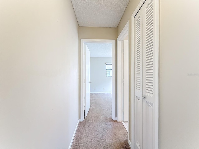 hallway featuring a textured ceiling, baseboards, and carpet flooring