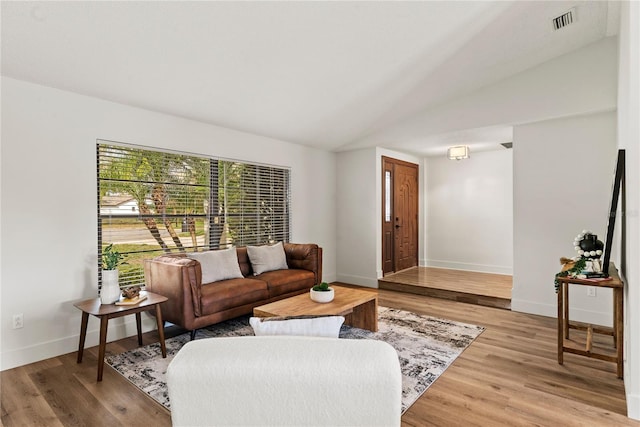 living area with light wood-style floors, visible vents, vaulted ceiling, and baseboards