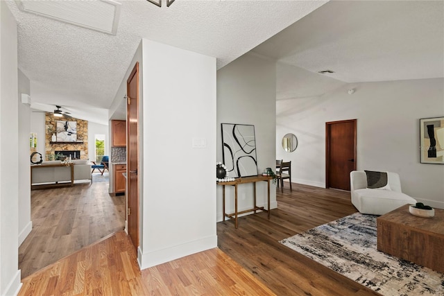 corridor with lofted ceiling, visible vents, a textured ceiling, and light wood-style flooring