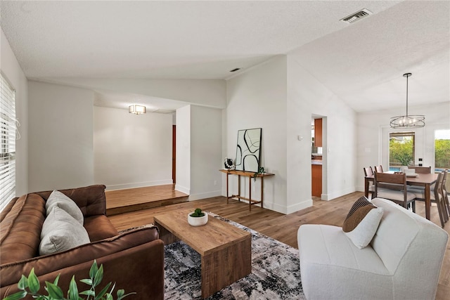 living room featuring lofted ceiling, light wood finished floors, visible vents, and an inviting chandelier