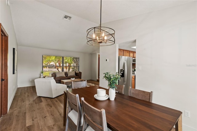 dining room with baseboards, visible vents, lofted ceiling, wood finished floors, and a chandelier