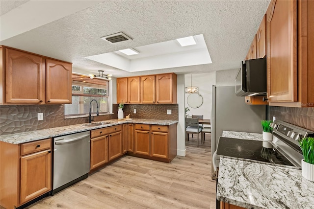 kitchen featuring a raised ceiling, light wood-style flooring, appliances with stainless steel finishes, brown cabinetry, and a sink