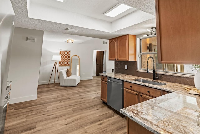 kitchen with light wood-style flooring, a sink, a textured ceiling, light stone countertops, and dishwasher