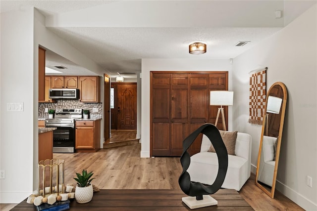 interior space with stainless steel appliances, light wood-type flooring, a textured ceiling, and decorative backsplash