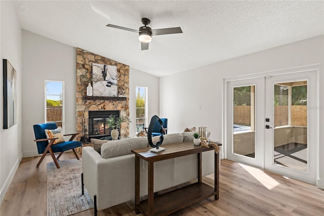 living area featuring lofted ceiling, wood finished floors, a stone fireplace, and french doors