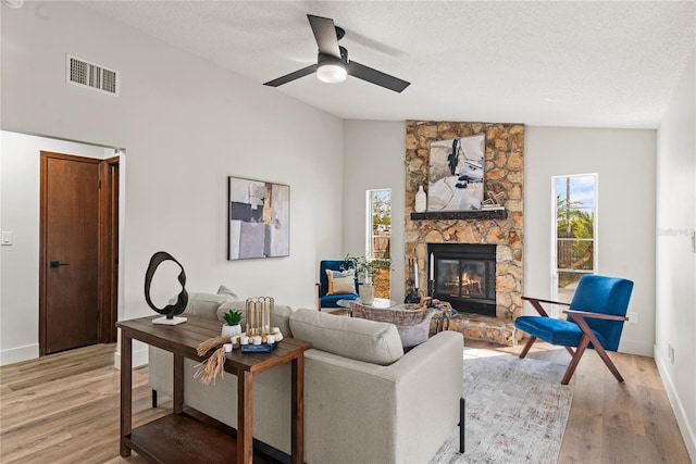 living room with vaulted ceiling, a stone fireplace, visible vents, and light wood-style floors