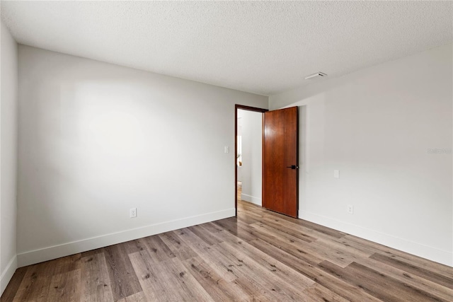 spare room with a textured ceiling, wood finished floors, visible vents, and baseboards