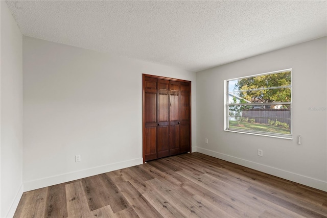 unfurnished bedroom with a closet, a textured ceiling, baseboards, and wood finished floors