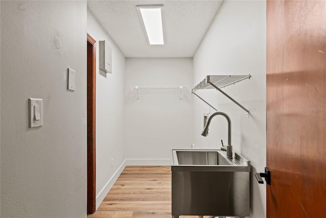 interior space featuring light wood-style flooring, a sink, a textured ceiling, laundry area, and baseboards