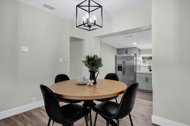 dining space with light wood-type flooring, baseboards, visible vents, and a notable chandelier