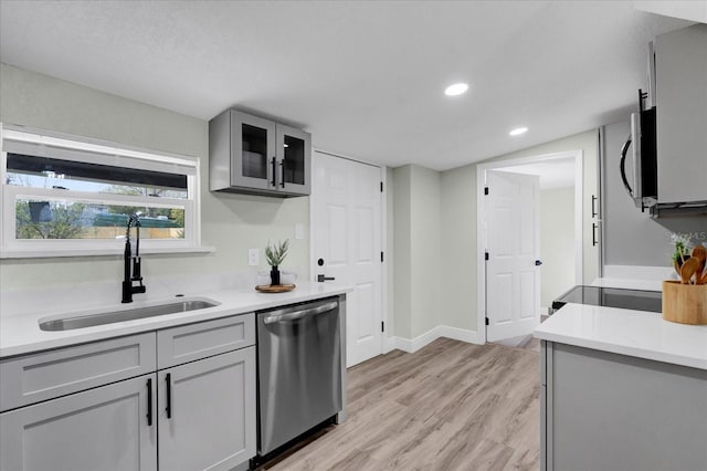 kitchen with appliances with stainless steel finishes, light countertops, a sink, and gray cabinetry