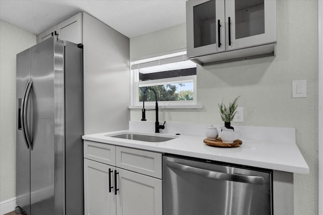 kitchen with stainless steel appliances, glass insert cabinets, white cabinetry, a sink, and light stone countertops