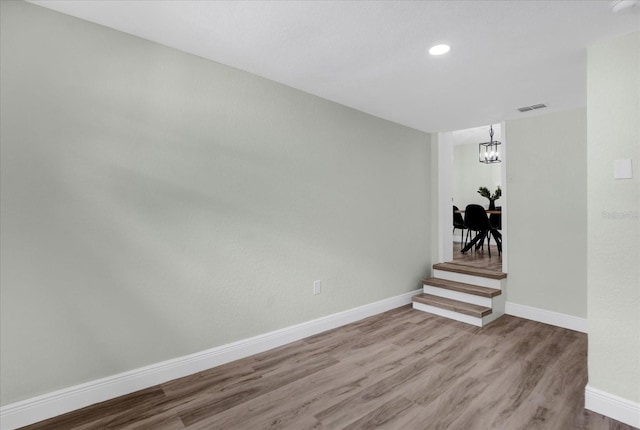 spare room with a notable chandelier, recessed lighting, wood finished floors, visible vents, and baseboards