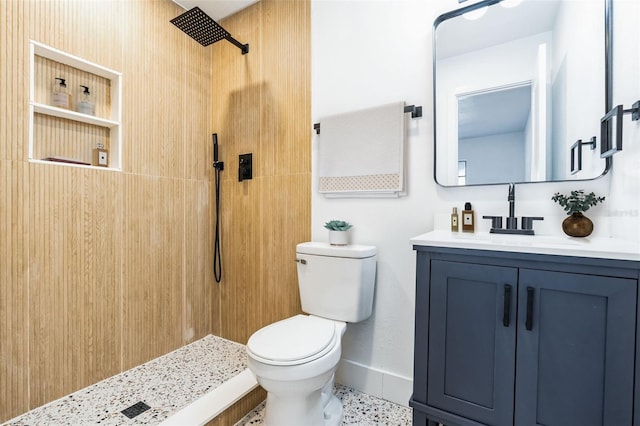 bathroom featuring toilet, baseboards, a tile shower, and vanity