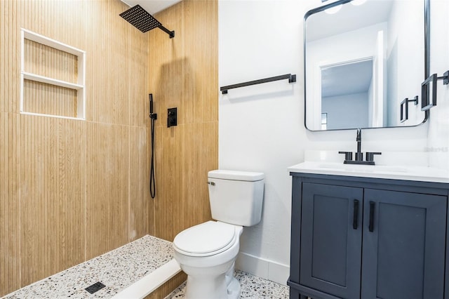 bathroom with baseboards, a tile shower, vanity, and toilet