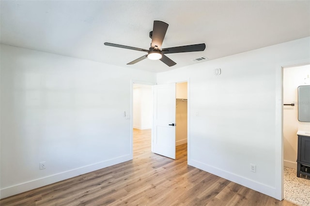 unfurnished bedroom featuring a walk in closet, light wood finished floors, a closet, visible vents, and baseboards