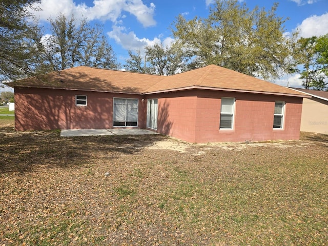 rear view of house with concrete block siding, a patio, and a lawn