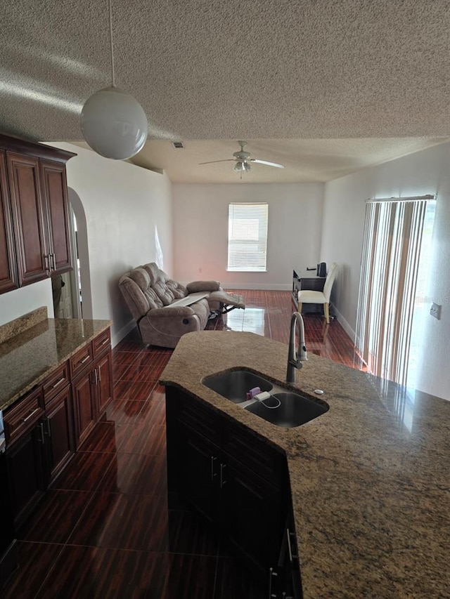 kitchen with arched walkways, a textured ceiling, wood finish floors, a sink, and a ceiling fan