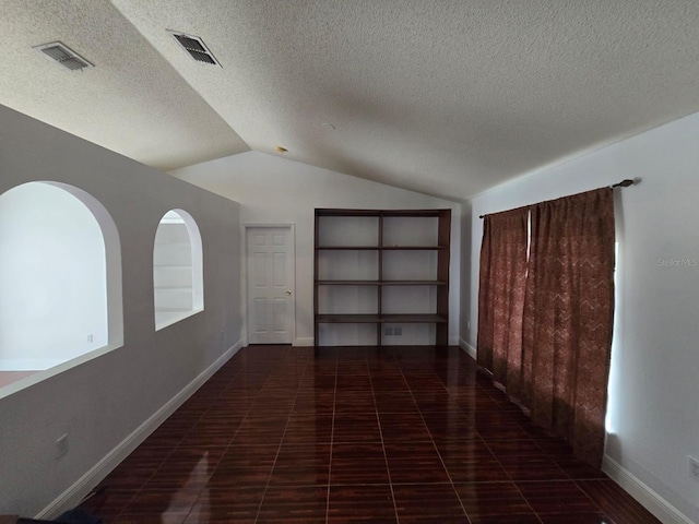 unfurnished room with vaulted ceiling, a textured ceiling, visible vents, and baseboards