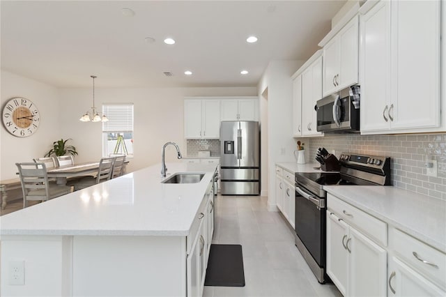 kitchen featuring white cabinets, hanging light fixtures, a kitchen island with sink, stainless steel appliances, and a sink