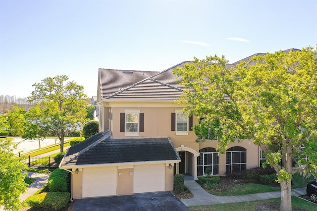 view of front of home with an attached garage, a tile roof, aphalt driveway, and stucco siding