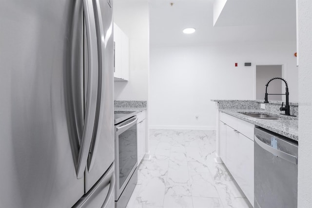 kitchen featuring marble finish floor, stainless steel appliances, white cabinets, a sink, and light stone countertops