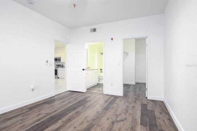 unfurnished bedroom featuring baseboards, visible vents, connected bathroom, dark wood finished floors, and a walk in closet