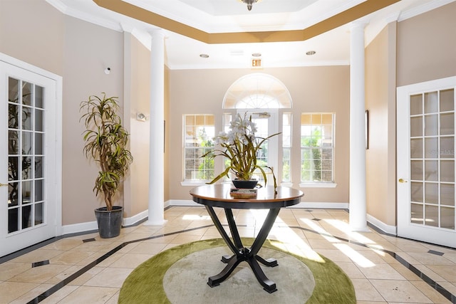 tiled foyer featuring ornamental molding, a raised ceiling, decorative columns, and baseboards