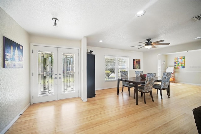 dining room with french doors, a textured wall, a textured ceiling, and light wood finished floors