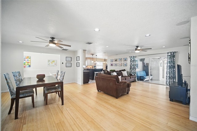 living area featuring a ceiling fan, light wood-type flooring, visible vents, and a textured ceiling