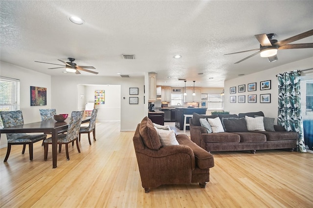 living room featuring light wood-style floors, visible vents, a textured ceiling, and a ceiling fan