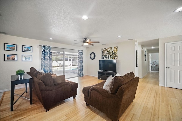 living area featuring a ceiling fan, light wood-style flooring, baseboards, and a textured ceiling