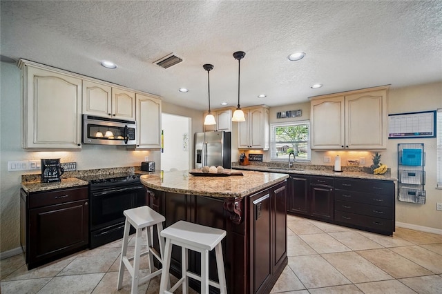 kitchen featuring visible vents, a center island, light stone countertops, stainless steel appliances, and a sink