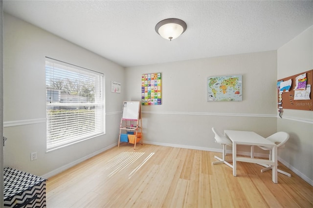 rec room with a textured ceiling, baseboards, and wood finished floors