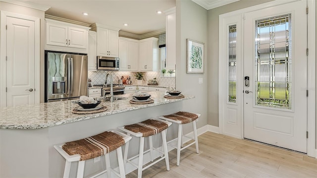 kitchen with tasteful backsplash, white cabinets, appliances with stainless steel finishes, light stone countertops, and light wood-type flooring