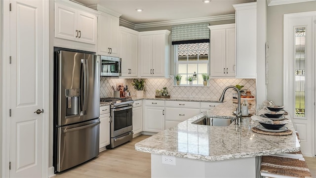 kitchen with light wood finished floors, light stone counters, stainless steel appliances, white cabinetry, and a sink