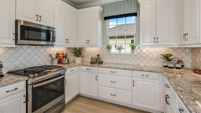 kitchen featuring light stone counters, light wood finished floors, stainless steel appliances, decorative backsplash, and white cabinets