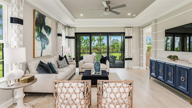 living area with a tray ceiling, light wood-type flooring, a ceiling fan, and crown molding