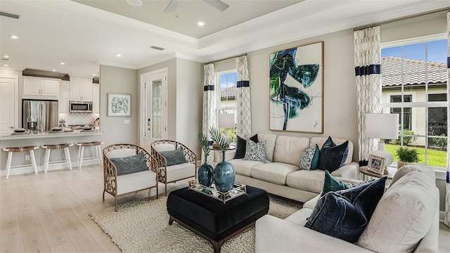 living room featuring recessed lighting, visible vents, light wood finished floors, a tray ceiling, and crown molding