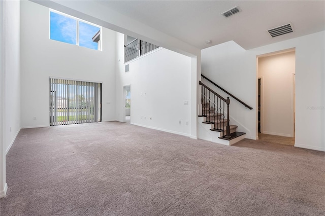 unfurnished living room with a high ceiling, visible vents, stairway, and carpet flooring