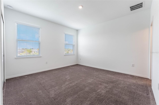 empty room with dark carpet, plenty of natural light, and visible vents