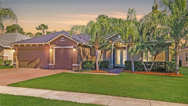 ranch-style house featuring stucco siding, french doors, a garage, decorative driveway, and a lawn