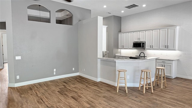 kitchen with stainless steel microwave, a kitchen breakfast bar, visible vents, and wood finished floors