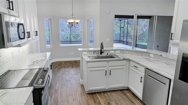 kitchen featuring dark wood finished floors, appliances with stainless steel finishes, a peninsula, white cabinetry, and a sink