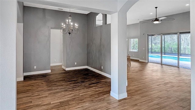 unfurnished dining area with baseboards, ceiling fan with notable chandelier, a high ceiling, wood finished floors, and arched walkways