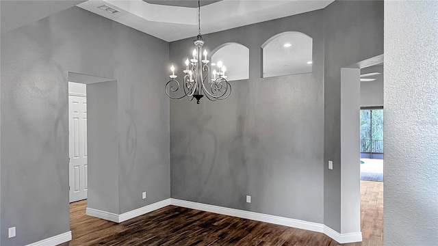 empty room featuring an inviting chandelier, wood finished floors, visible vents, and baseboards