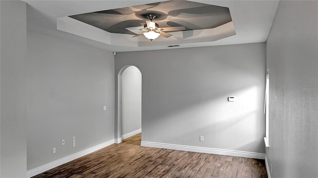 unfurnished room with baseboards, a raised ceiling, arched walkways, and wood finished floors