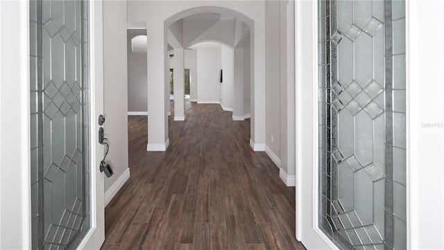 entryway featuring baseboards, arched walkways, and dark wood finished floors