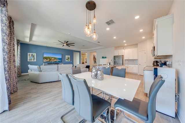 dining room with visible vents, a ceiling fan, a tray ceiling, light wood-style floors, and recessed lighting