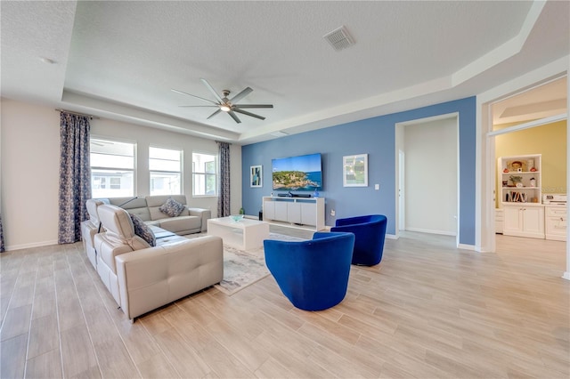 living room with a textured ceiling, visible vents, baseboards, light wood finished floors, and a tray ceiling